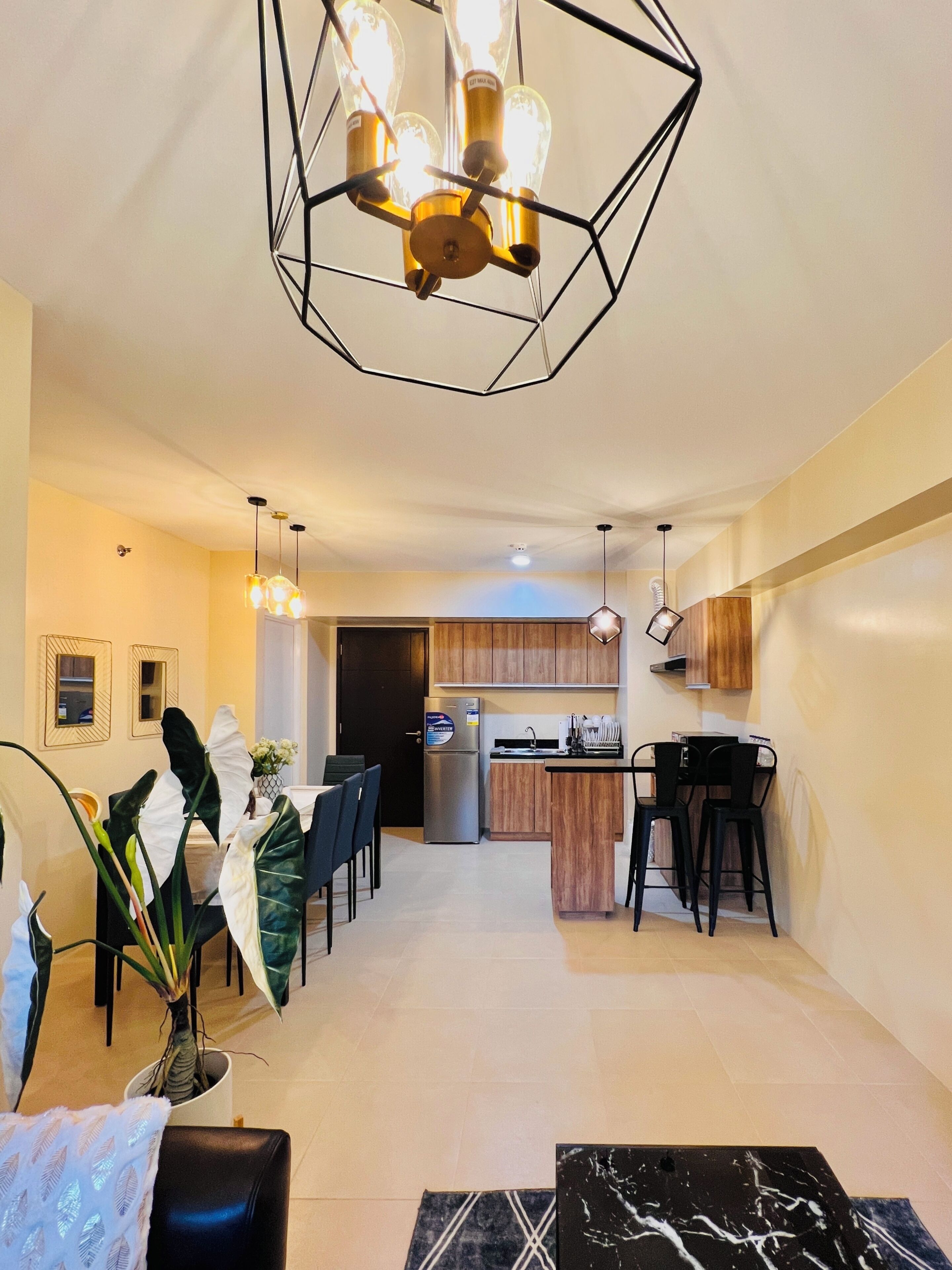 A modern kitchen with wooden cabinets, a stainless steel refrigerator, and a dining area with a table and chairs.