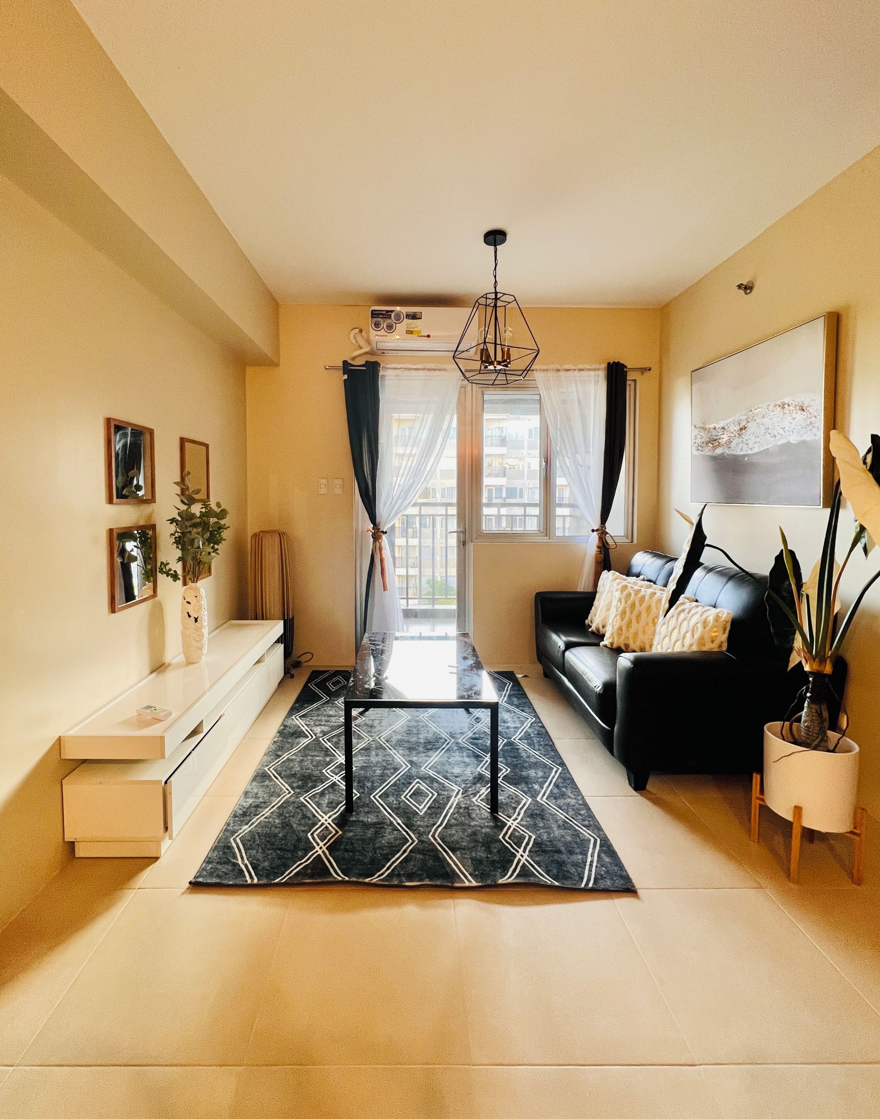 Un salon moderne avec un canapé noir, une table basse et une grande fenêtre agrémentée de rideaux.