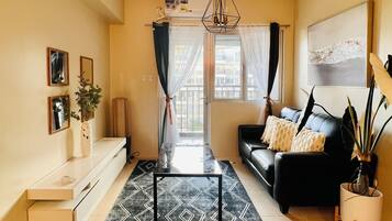 A modern living room with a black sofa, a coffee table, and a large window with curtains.
