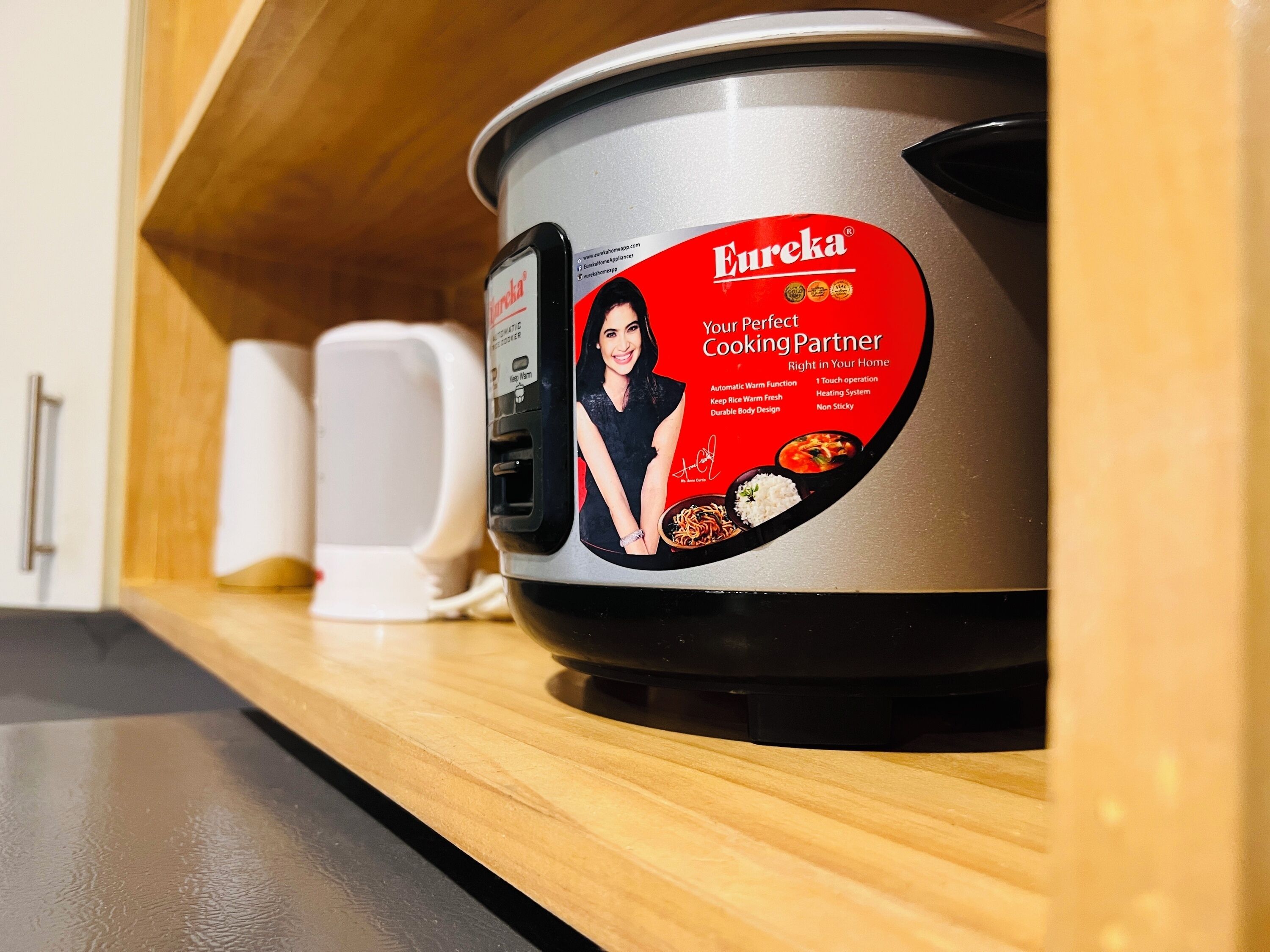A kitchen with a stainless steel pot labeled 'Eureka Your Perfect Cooking Partner' on a wooden shelf.