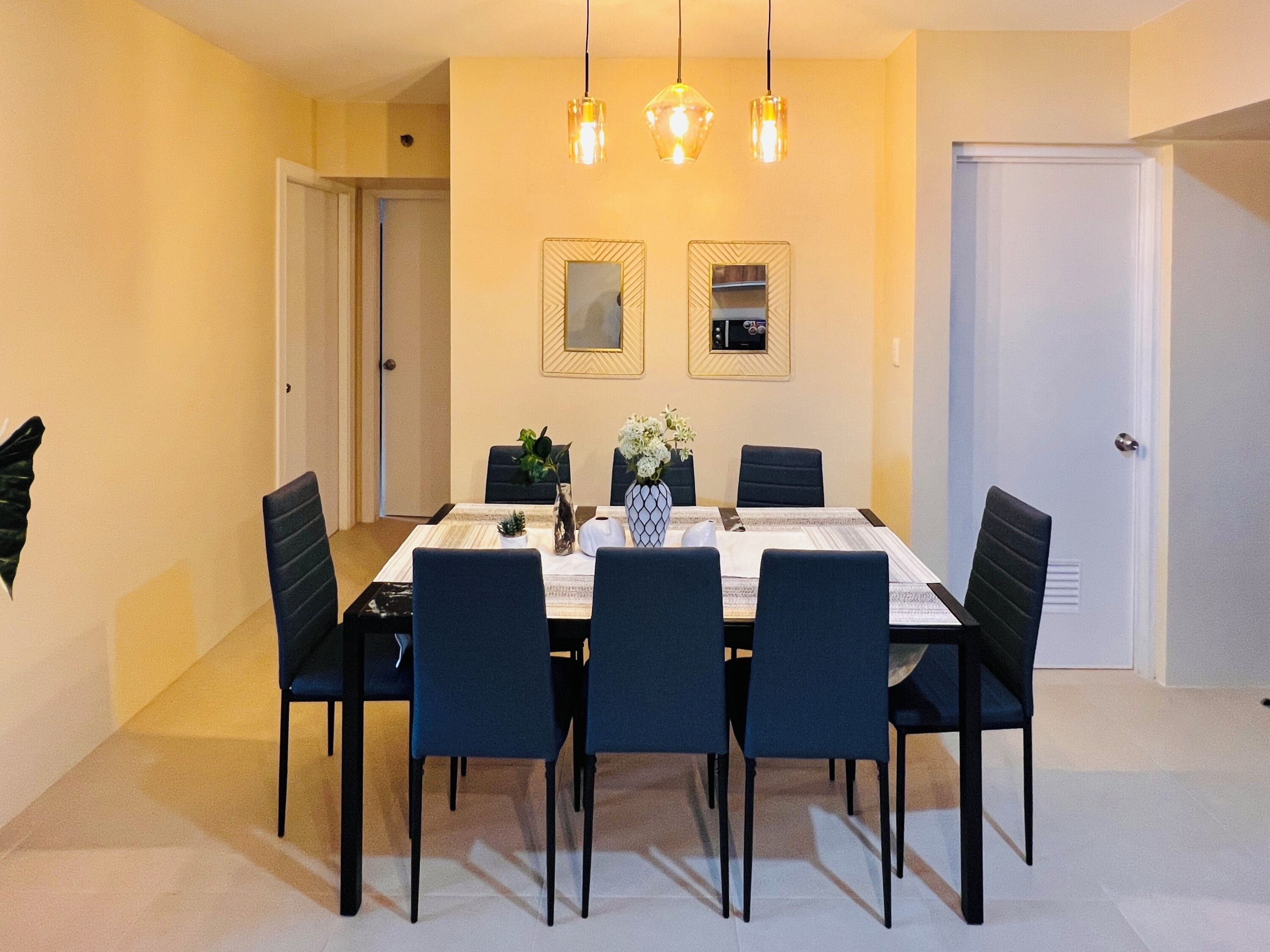 Une salle à manger avec une table rectangulaire, six chaises, un vase de fleurs et deux miroirs fixés au mur.
