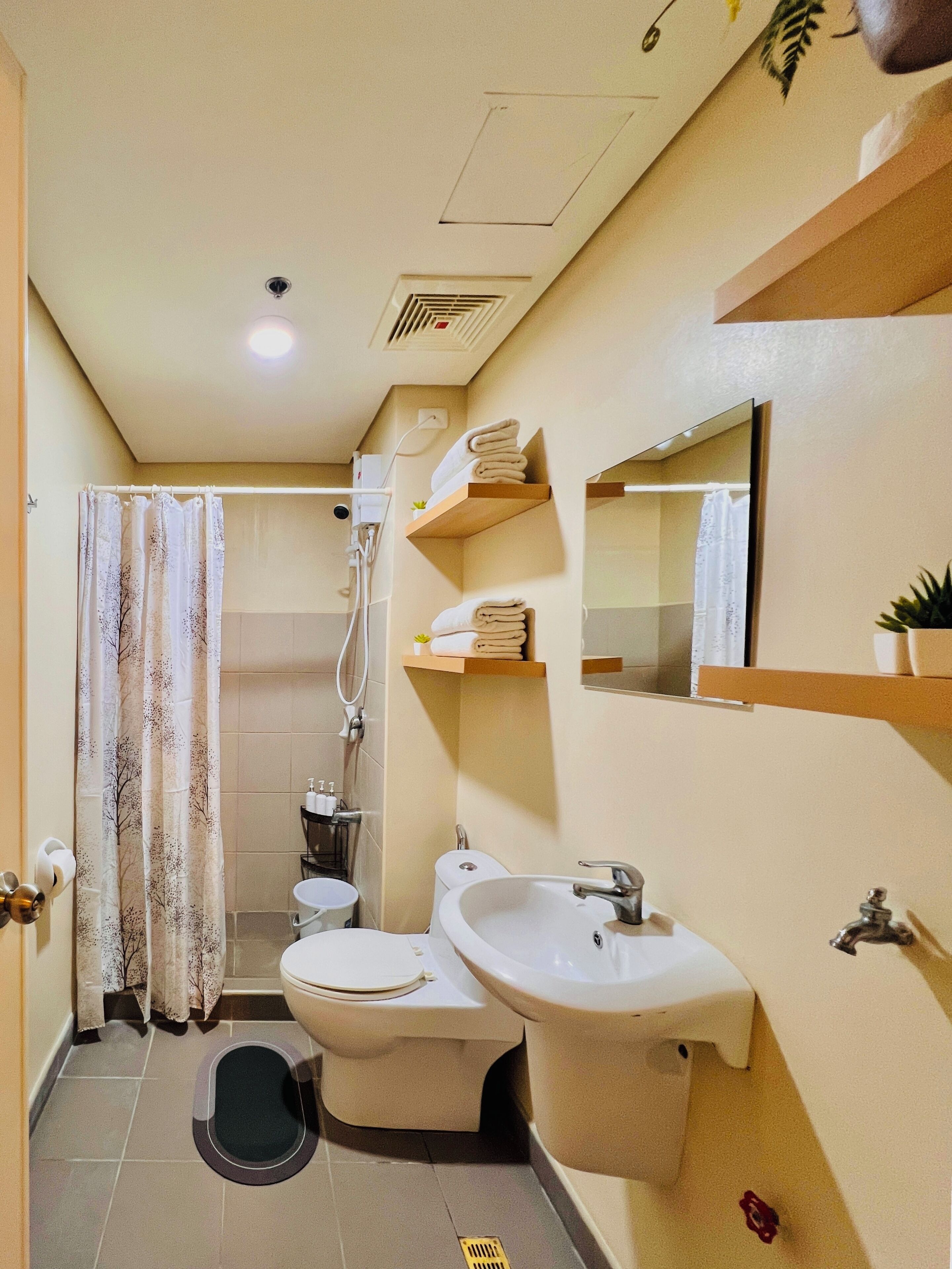 A compact bathroom with a toilet, bidet, and sink. There are shelves with towels and a small plant.