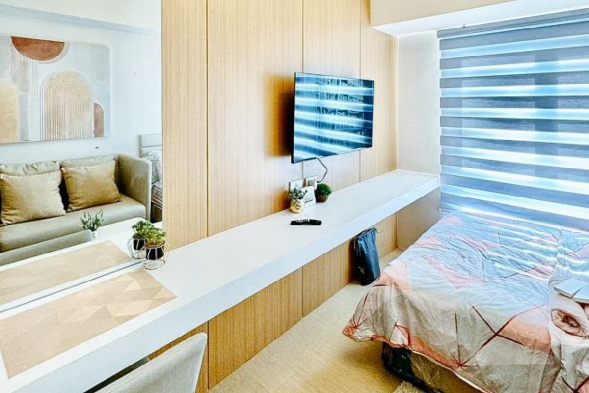 A modern bedroom with a bed, a mounted TV, a bedside table, and a window with blinds.