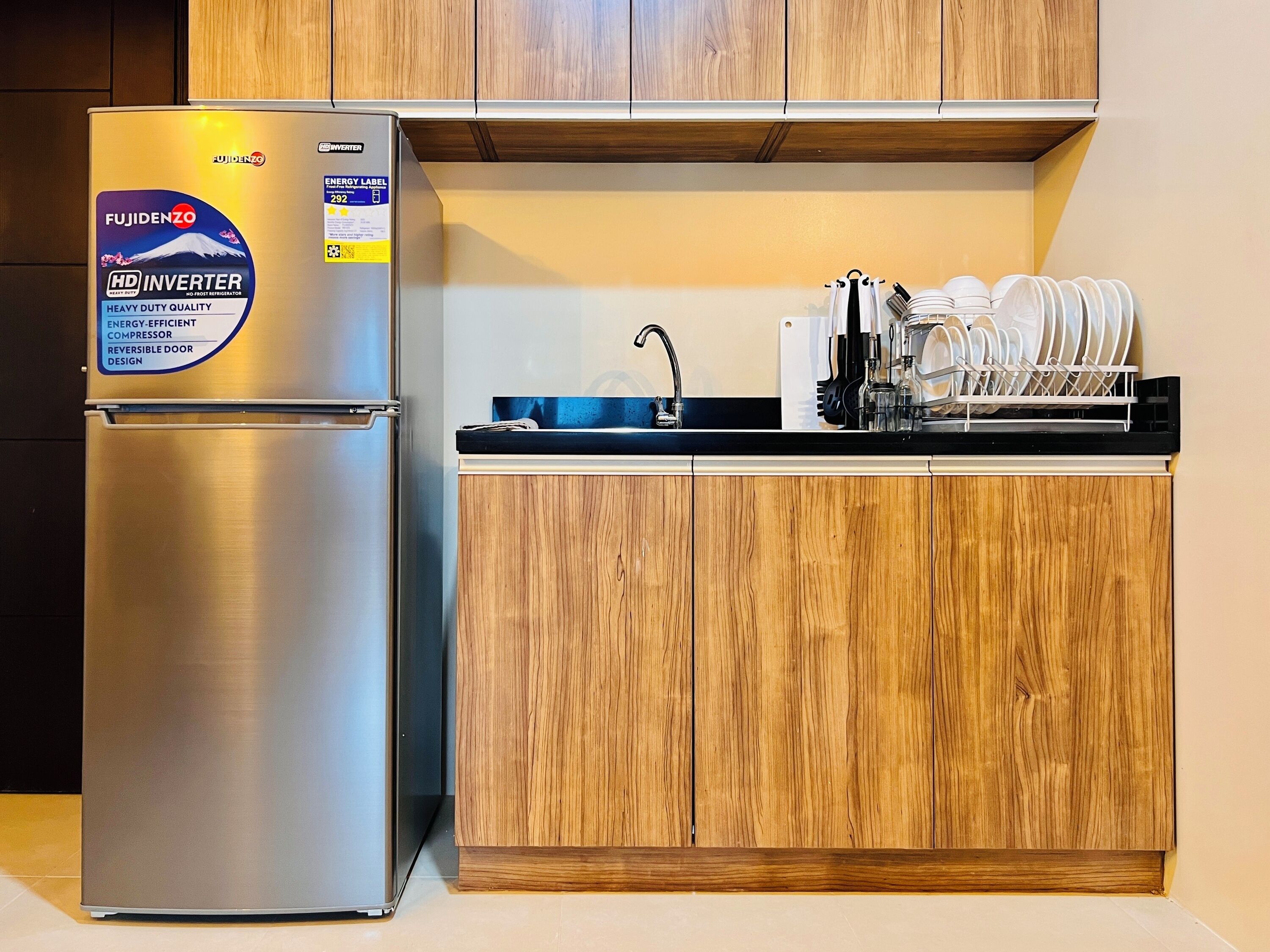 A compact kitchen with a stainless steel refrigerator, wooden cabinets, and a dish drying rack.