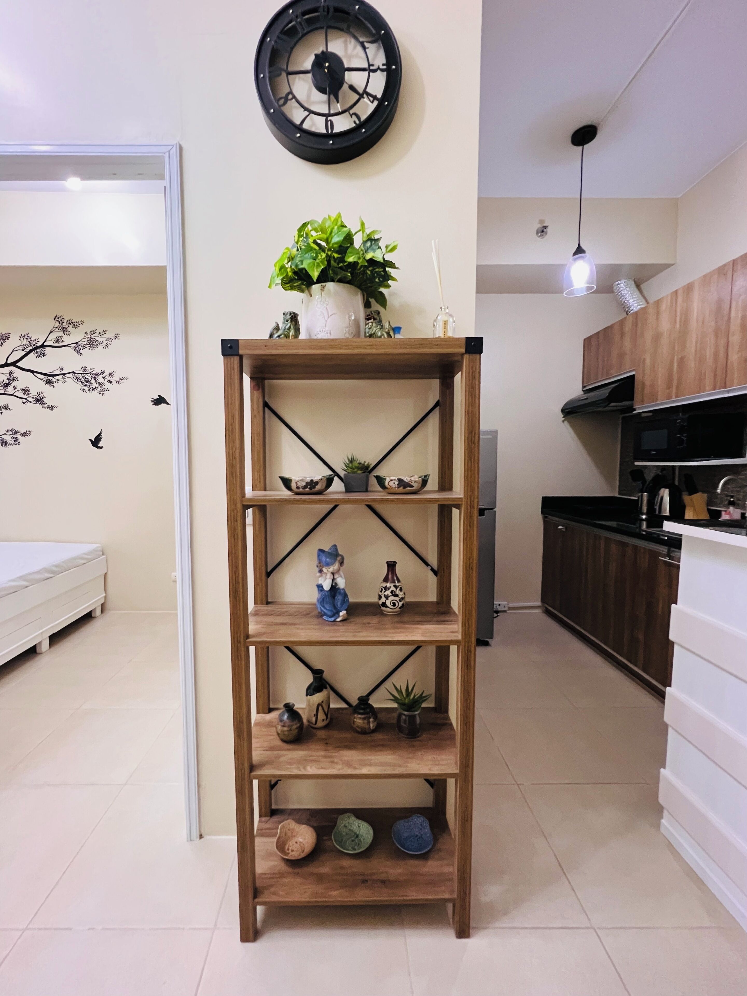 A wooden bookshelf with decorative items, a wall clock, and a potted plant in a modern living space.
