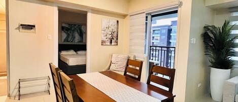 A dining area with a wooden table and chairs, a white tablecloth, and a painting on the wall.