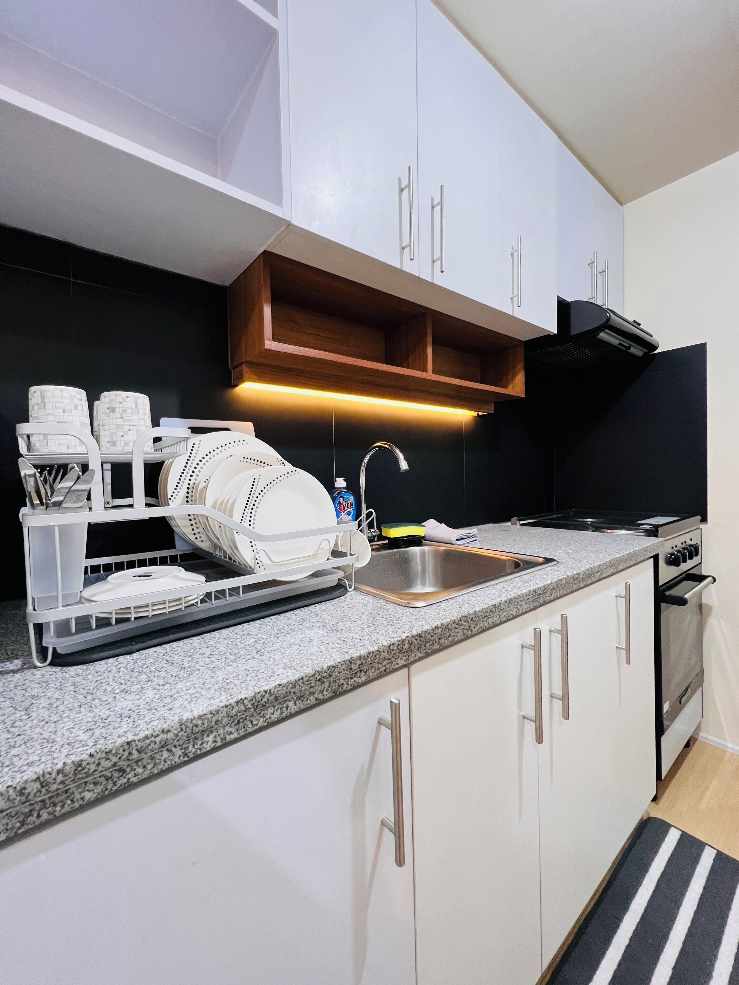 A kitchen with white cabinets, a granite countertop, a stainless steel sink, and a black range hood.