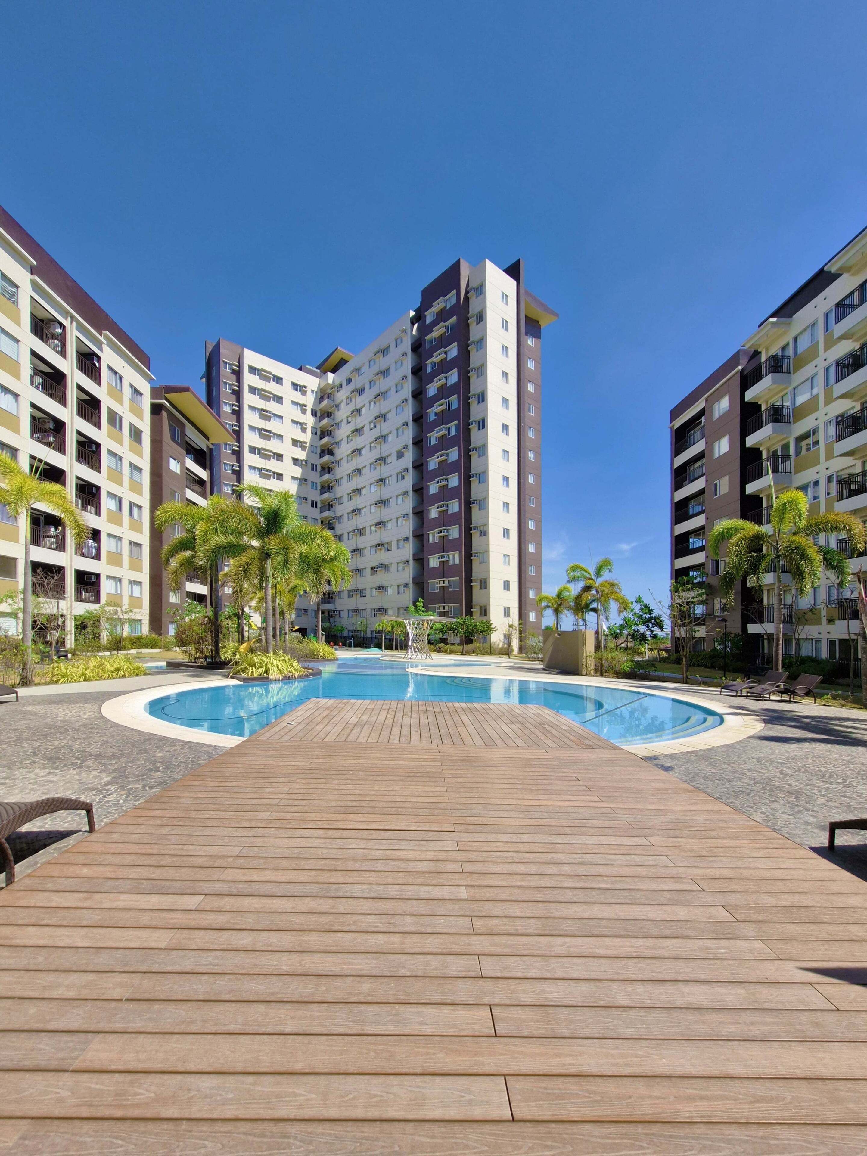 A modern hotel with a central swimming pool, surrounded by a wooden deck and palm trees.