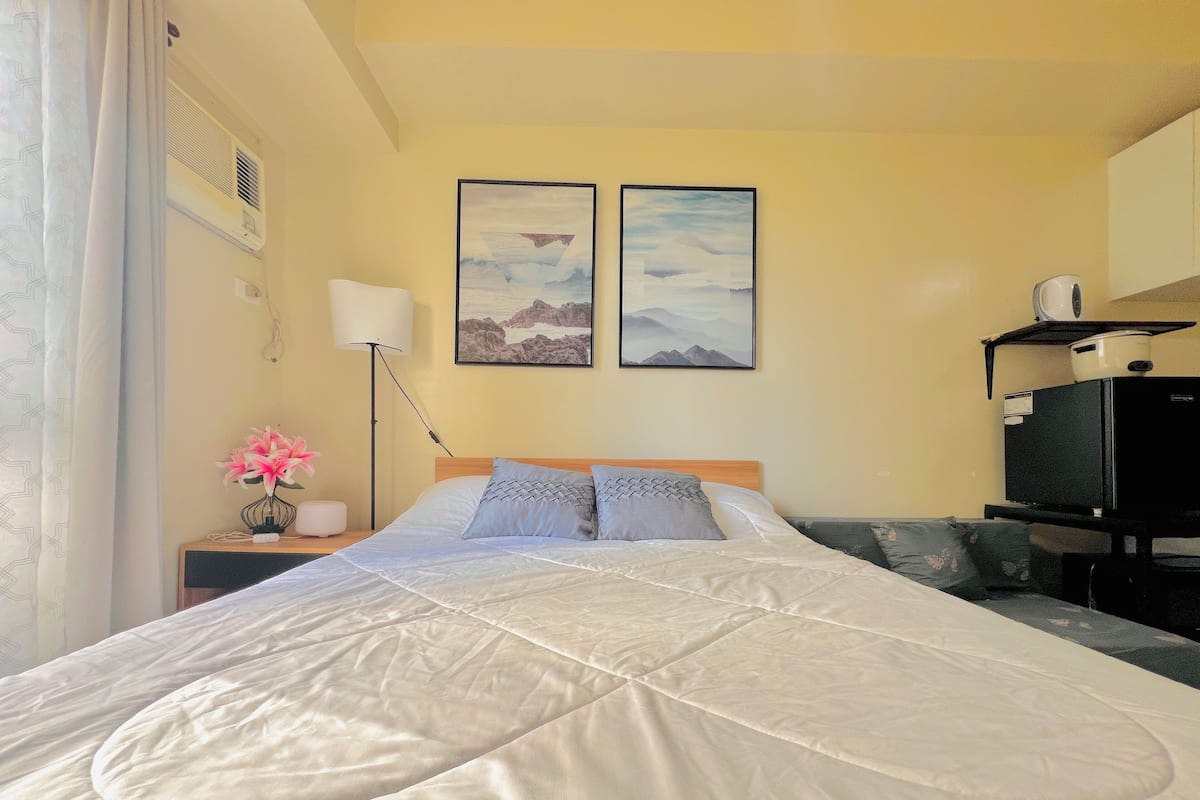 A hotel room with a bed, a nightstand, a lamp, a TV, and two framed pictures on the wall.