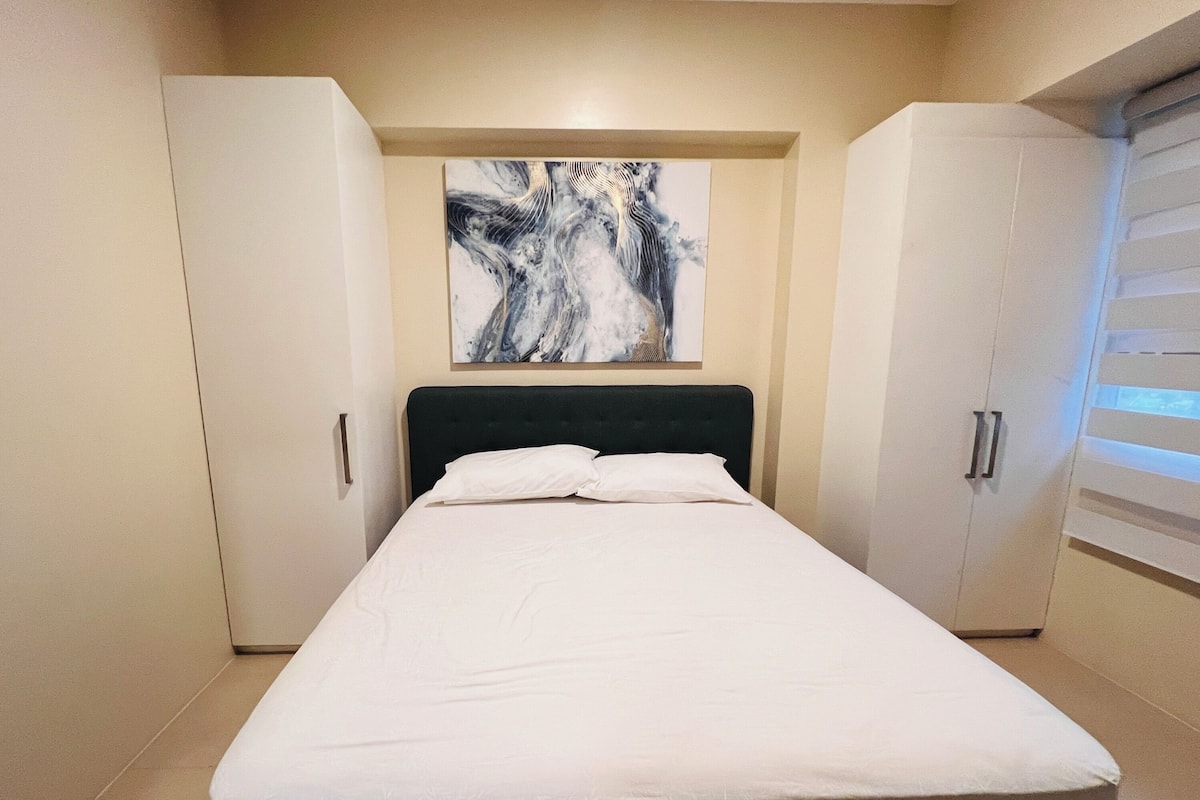 A bedroom with a bed, a painting on the wall, and a wardrobe.