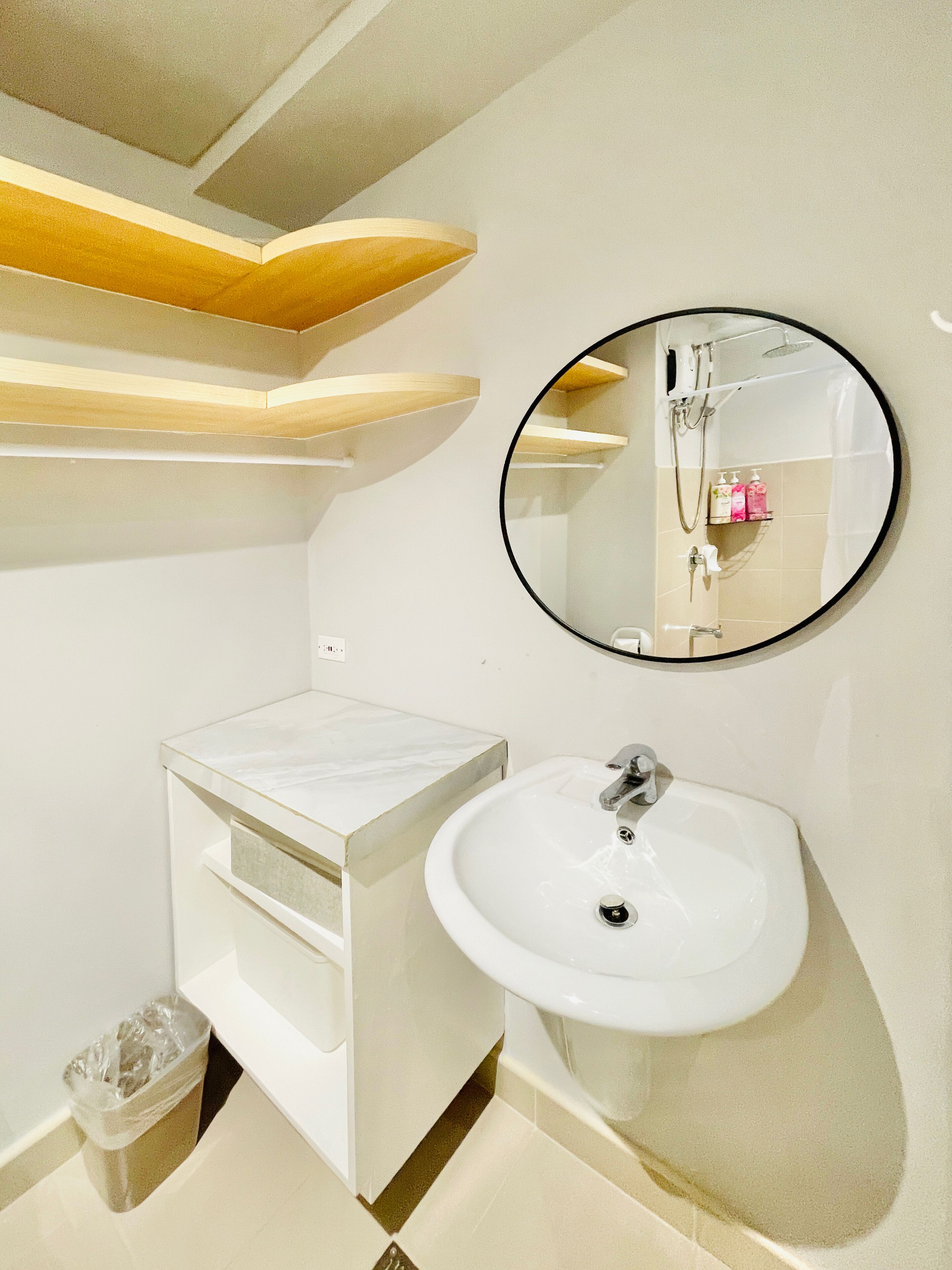 A modern bathroom with a white sink, a round mirror, and wooden shelves.