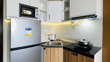 A compact kitchen with a refrigerator, microwave, stove, and wooden cabinets.