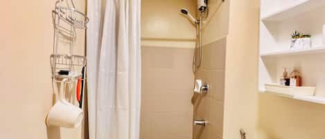 A small bathroom with a shower, toilet, and a shelf with toiletries.