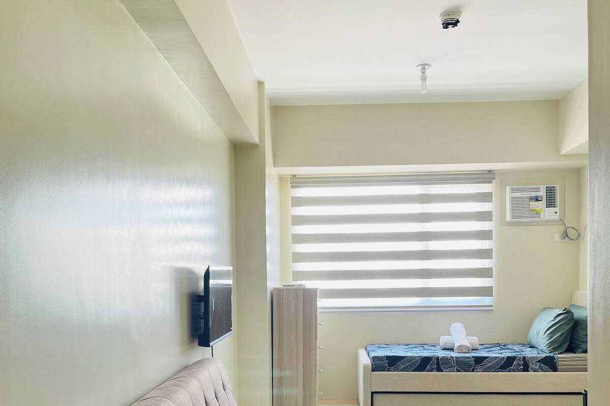 A room with a sofa, a bed, a wardrobe, and a window with blinds.