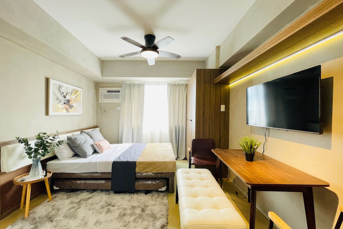 A modern bedroom with a bed, bedside table, bench, and a TV mounted on the wall.