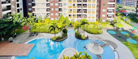Un edificio residencial de varios pisos con una piscina central rodeada de palmeras y follaje.