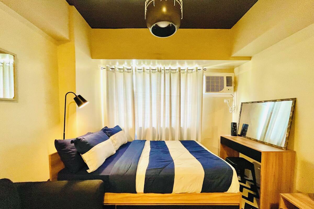 A bedroom with a bed, a bedside table, a lamp, a mirror, and a ceiling light fixture.