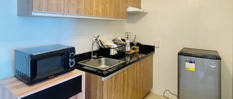 A compact kitchen with wooden cabinets, a built-in microwave, a sink, and a refrigerator.