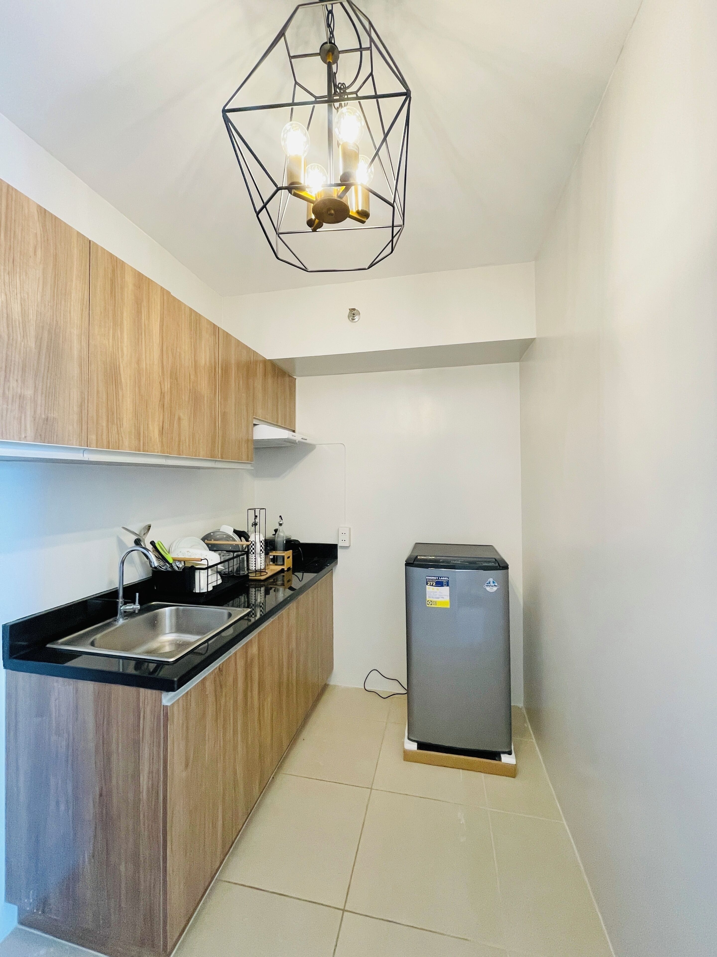 Une cuisine compacte dotée d’un plan de travail noir, de meubles en bois, d’un évier en acier inoxydable et d’un réfrigérateur encastré.