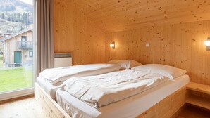 Habitación de cabaña de madera con dos camas, una ventana con cortinas y vista a un edificio.