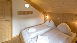 Un dormitorio con techo de madera, una cama con ropa blanca, una puerta de madera y una lámpara de pared.