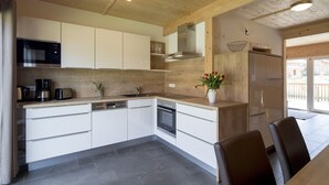 Una cocina moderna con armarios blancos, un microondas de acero inoxidable, una cafetera y un lavabo. Hay un florero con flores en la encimera y un refrigerador a la derecha.