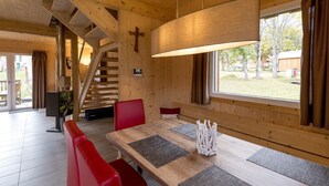 Un interior de madera con una escalera, una zona de comedor con sillas rojas, un ventanal grande y una cruz en la pared.