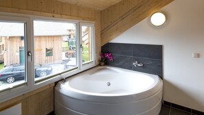 Un baño moderno con una bañera redonda grande, una ventana con vistas al exterior y una pared de azulejos oscuros.