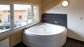 Een moderne badkamer met een groot, rond bad, een raam met uitzicht en een donkere betegelde muur.