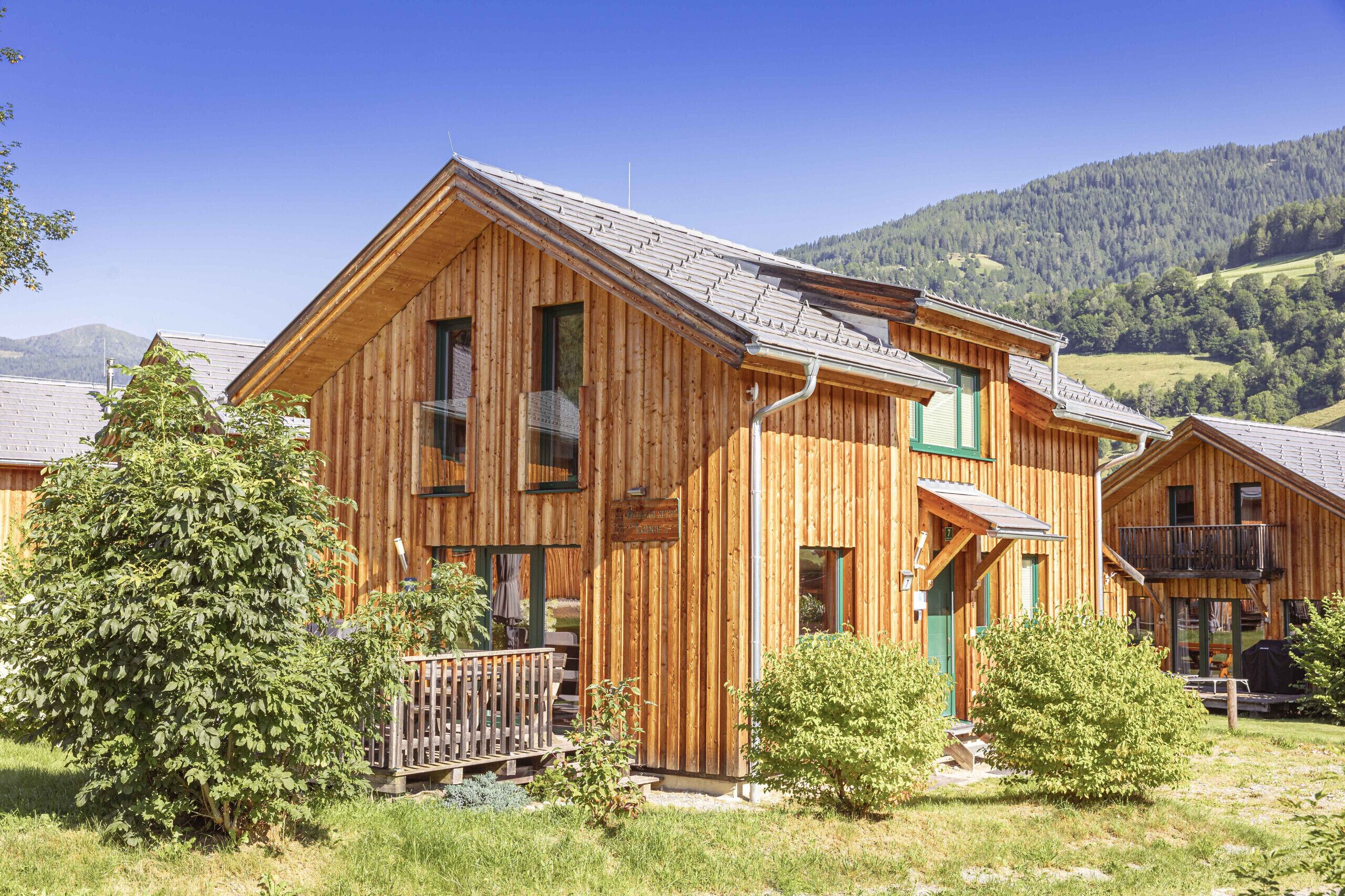 Een houten chalet met balkon, omringd door groen en bergen.