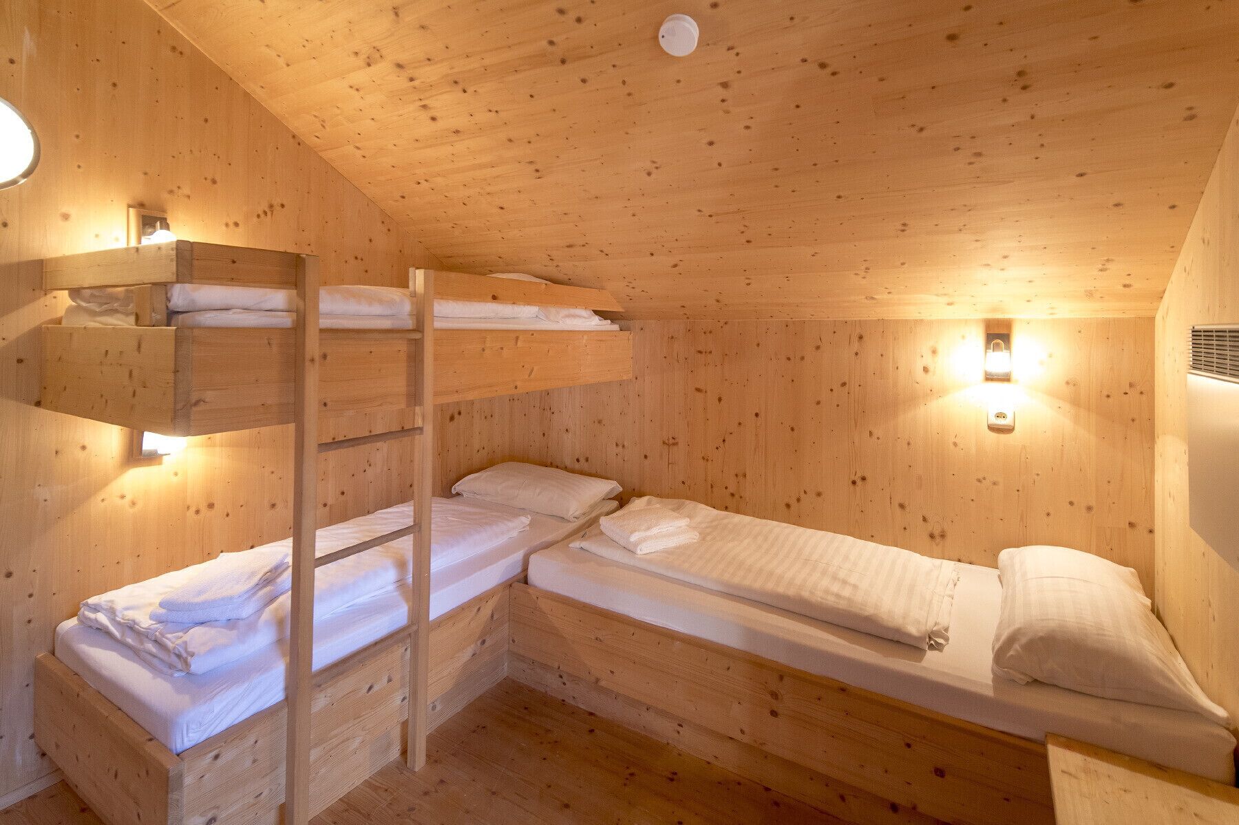 A cabin with wooden walls and floors, featuring two bunk beds and a single bed.