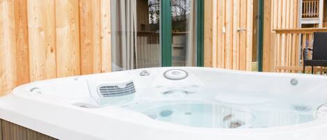 A hot tub in front of a wooden cabin with a glass door and a balcony.