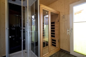 Habitación con cabina de ducha de vidrio, puerta de madera con ventana y puerta corredera de cristal que da al exterior.