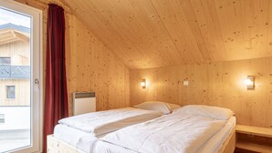 Camera in una baita di legno con due letti, una finestra con tenda rossa e vista su un edificio.