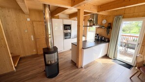 A modern kitchen with a wood stove, white cabinets, and a view of the outdoors through a glass door.