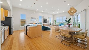 A modern kitchen with a central island, a dining area with a round table and chairs, and a living space with a sofa and a TV. - Seaside Cottages, 3 Homes, Pool, Beach & Golf Cart (Port Aransas)