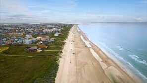 An aerial view of a coastal area with a long sandy beach, a row of colorful buildings, and a clear view of the ocean. - Seaside Cottages, 3 Homes, Pool, Beach & Golf Cart (Port Aransas)