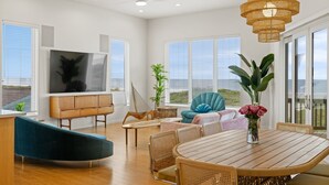 A spacious living area with a TV, comfortable seating, a dining table, and large windows. - Seaside Cottages, 3 Homes, Pool, Beach & Golf Cart (Port Aransas)