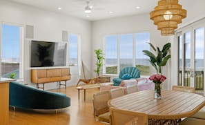 A spacious living area with a TV, comfortable seating, a dining table, and large windows. - Golf Cart, Pool & Beach | 3 Homes, Sleeps 22 - Seaside Cottages (Port Aransas)