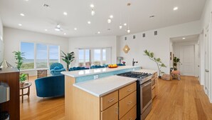 A modern kitchen with a central island, wooden cabinets, and a view to the outside. - Seaside Cottages, 3 Homes, Pool, Beach & Golf Cart (Port Aransas)