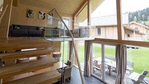 A modern interior with a wooden staircase, a sofa, and a glass railing overlooking a deck.