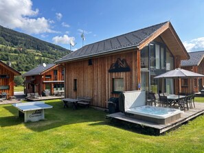 A wooden cabin with a hot tub, outdoor seating, and a mountain view.