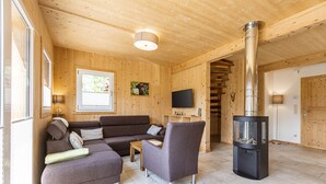 A wooden interior with a sofa, armchair, and a wood-burning stove.
