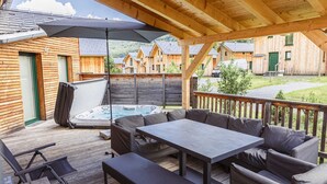 A wooden deck with a hot tub, outdoor seating, and a covered area with a table and chairs.