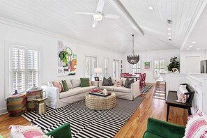 A spacious living room with a high ceiling, a large window, a sofa set, a coffee table, and a dining area.