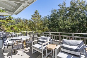 A balcony with outdoor furniture, including a table, chairs, and a sofa, surrounded by a white railing.