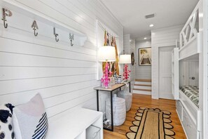 Un pasillo con pared blanca, un banco, una mesa con lámparas y una escalera que conduce a un dormitorio.