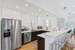 A modern kitchen with stainless steel appliances, white cabinetry, and a bar area with stools.