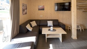 Una habitación acogedora con un sofá marrón oscuro, una mesa de centro de madera y un televisor de pantalla plana montado en la pared.