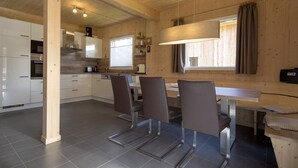 Una cocina moderna con armarios blancos, un comedor con mesa y sillas, y un amplio ventanal con cortinas.